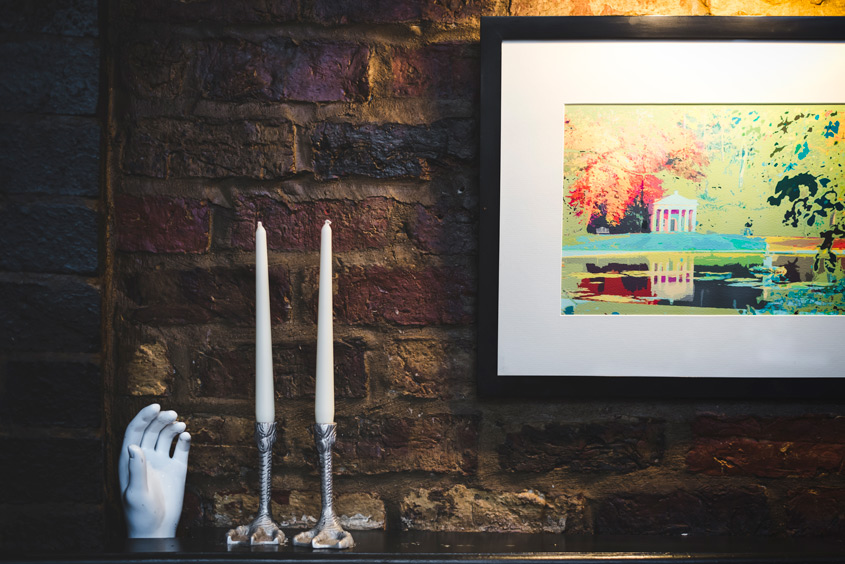 A corner of the bar at The Whippet Inn — a ceramic hand candle holder, silver
candlesticks and framed artwork on bare Victorian brick