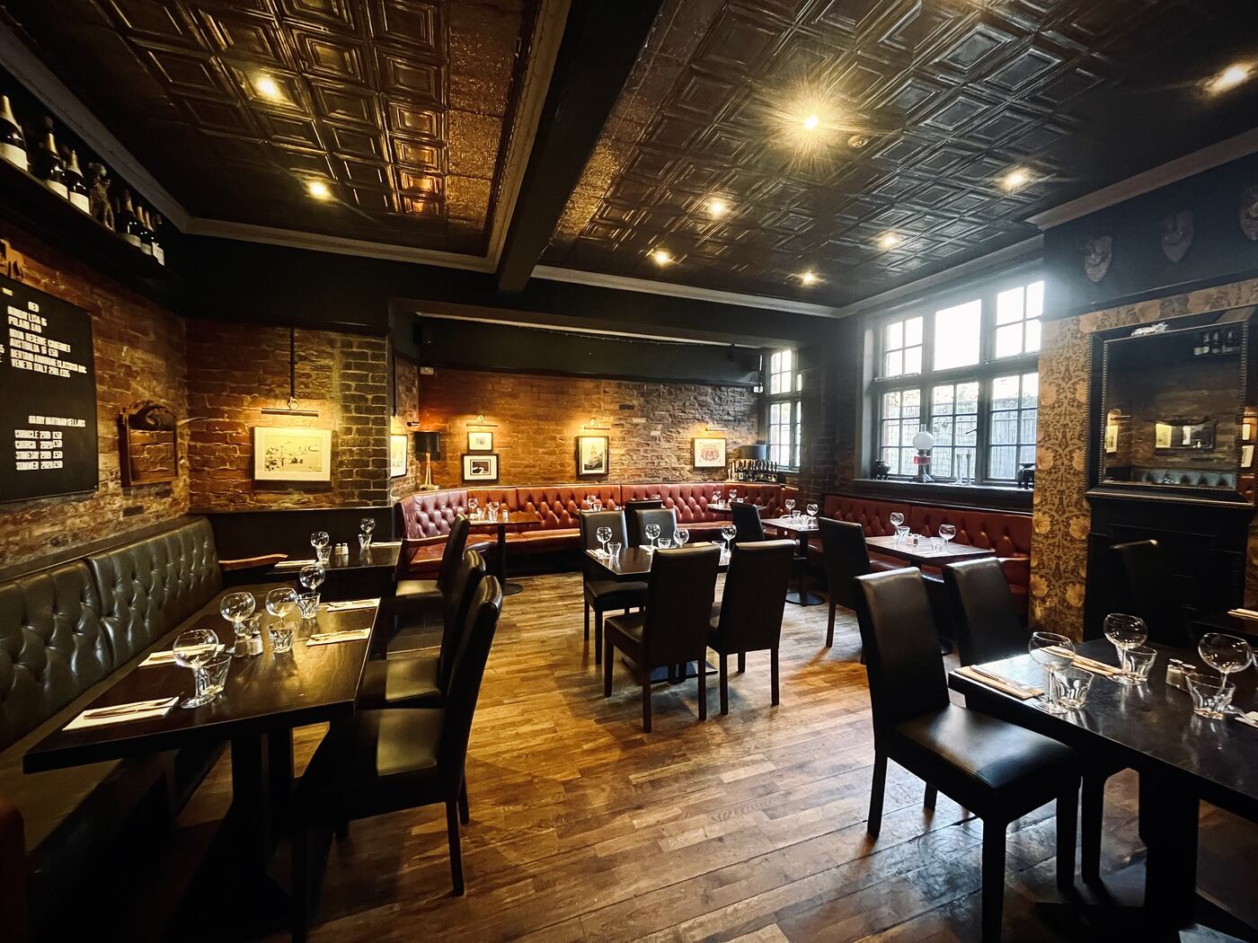The moody main dining room at The Whippet Inn — red leather banquettes, bare
brick and mullioned Victorian windows
