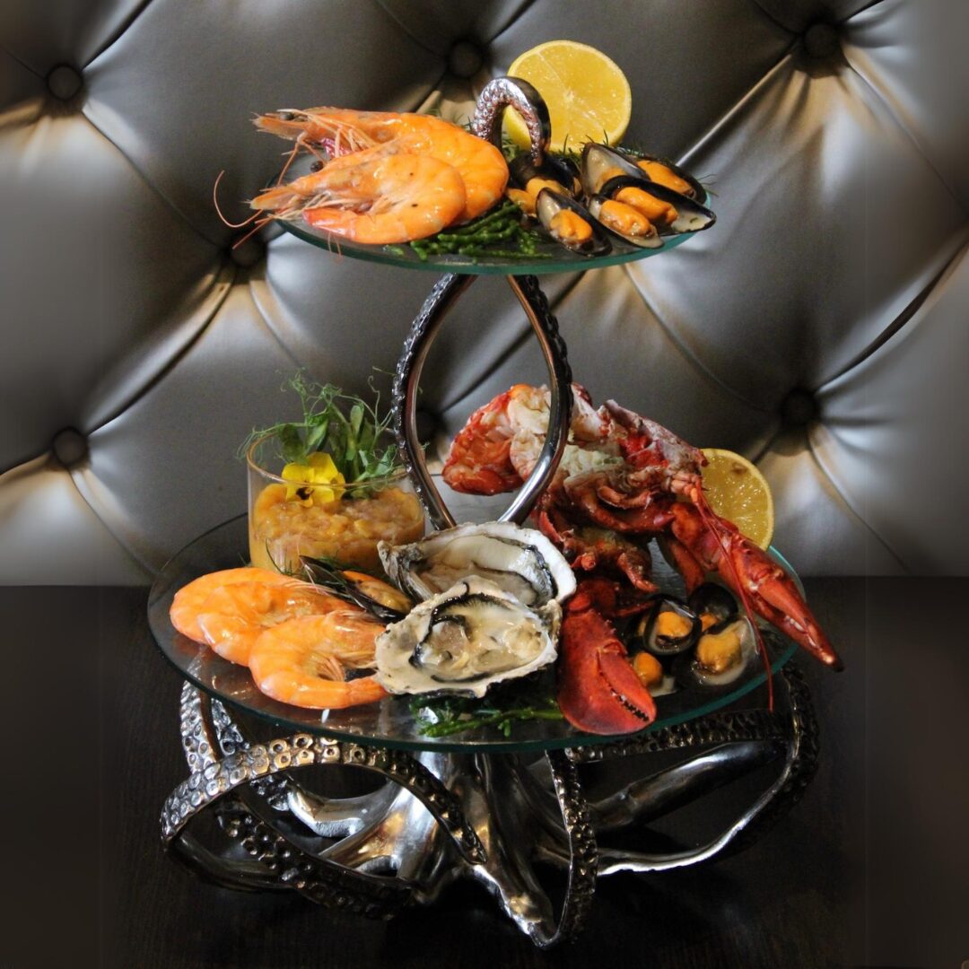 A two-tier seafood platter — prawns, mussels, oysters and lobster on ice —
set against a buttoned leather banquette at The Whippet Inn